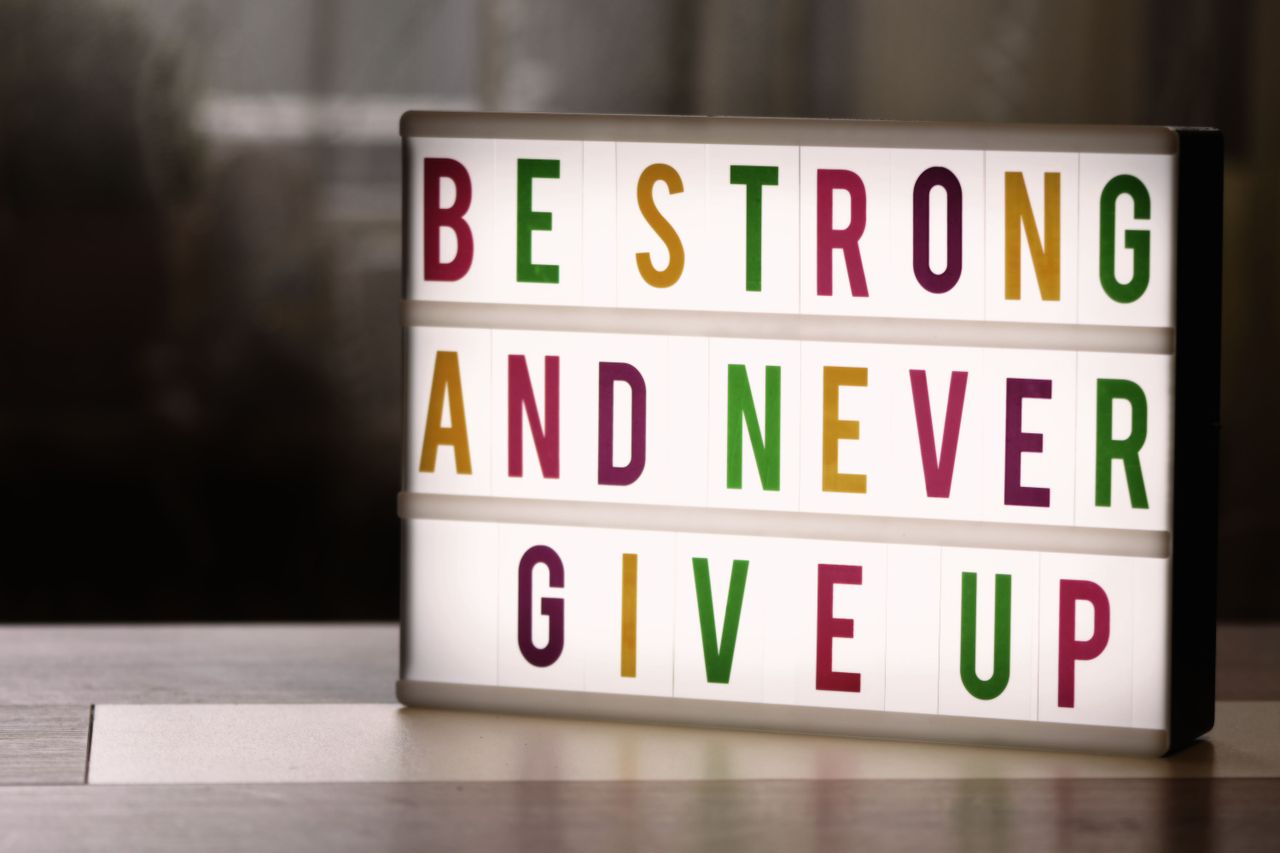 about-us-02 Inspirational lightbox displaying the motivational quote 'Be Strong and Never Give Up' indoors.