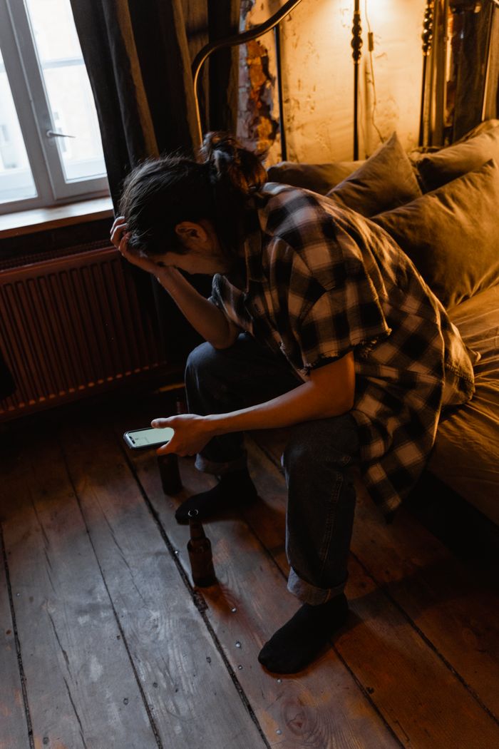 about-us-01 A young adult sits indoors, looking contemplative and holding a phone, creating a thoughtful mood.